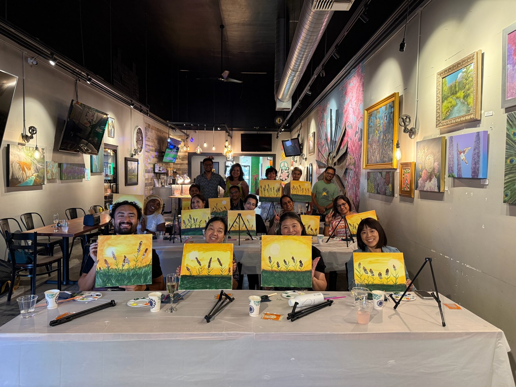 Participants smile at the camera while holding their paintings at the end of Brush Hour.