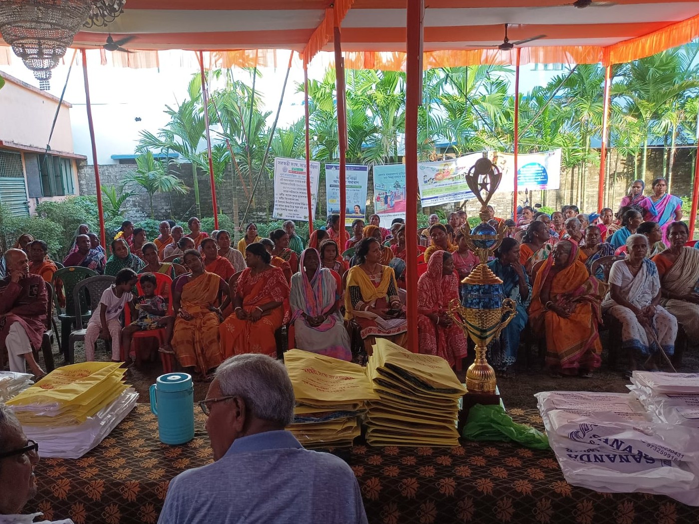 Community members and local organizers gather around clothing packages at a neighborhood event in West Bengal.